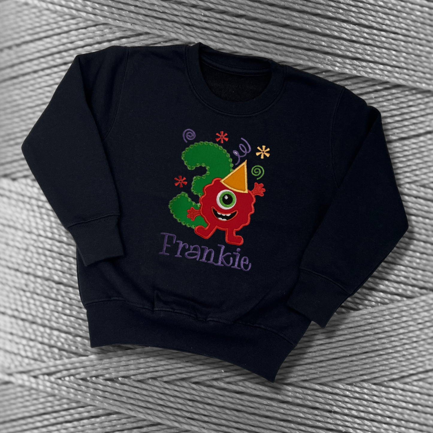 Childrens black sweatshirt with fleece lining. Embroidered applique on the front with the birthday age, funny monster design and the childs name.
