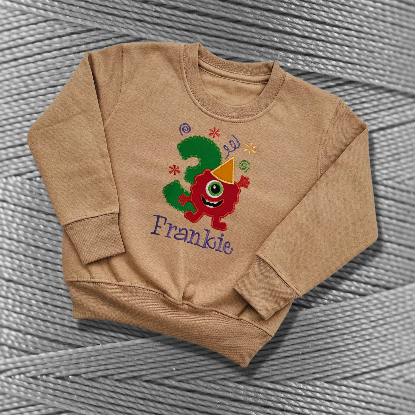 Childrens taupe sweatshirt with fleece lining. Embroidered applique on the front with the birthday age, funny monster design and the childs name.