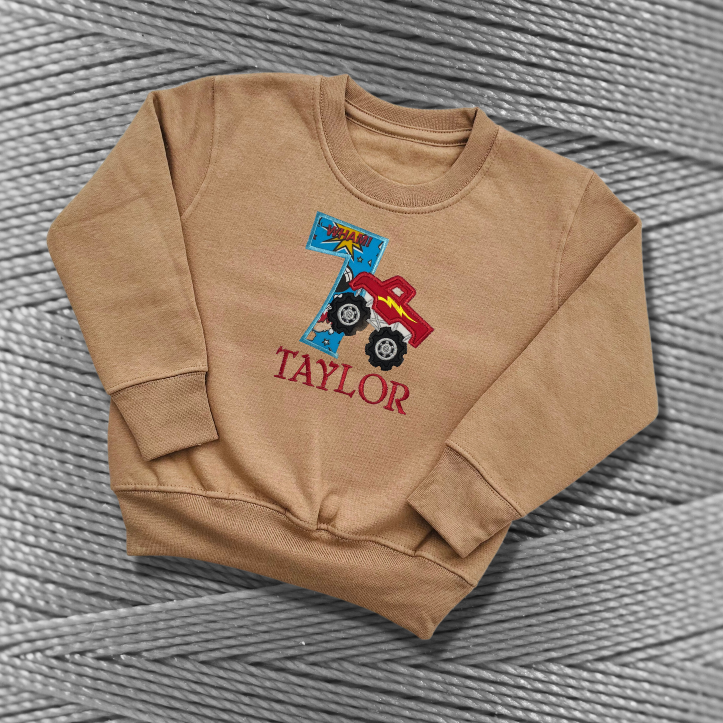 Childrens taupe sweatshirt with fleece lining. Embroidered applique on the front with the birthday age, monster truck design and the childs name.