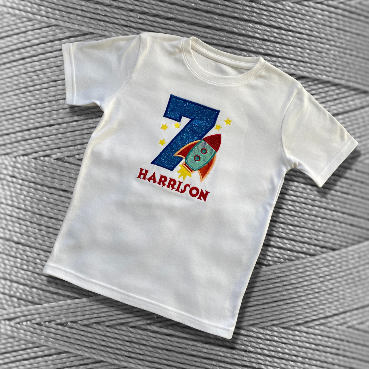 Childrens white soft cotton t-shirt. Embroidered applique on the front with the birthday age, rocket design and the childs name.