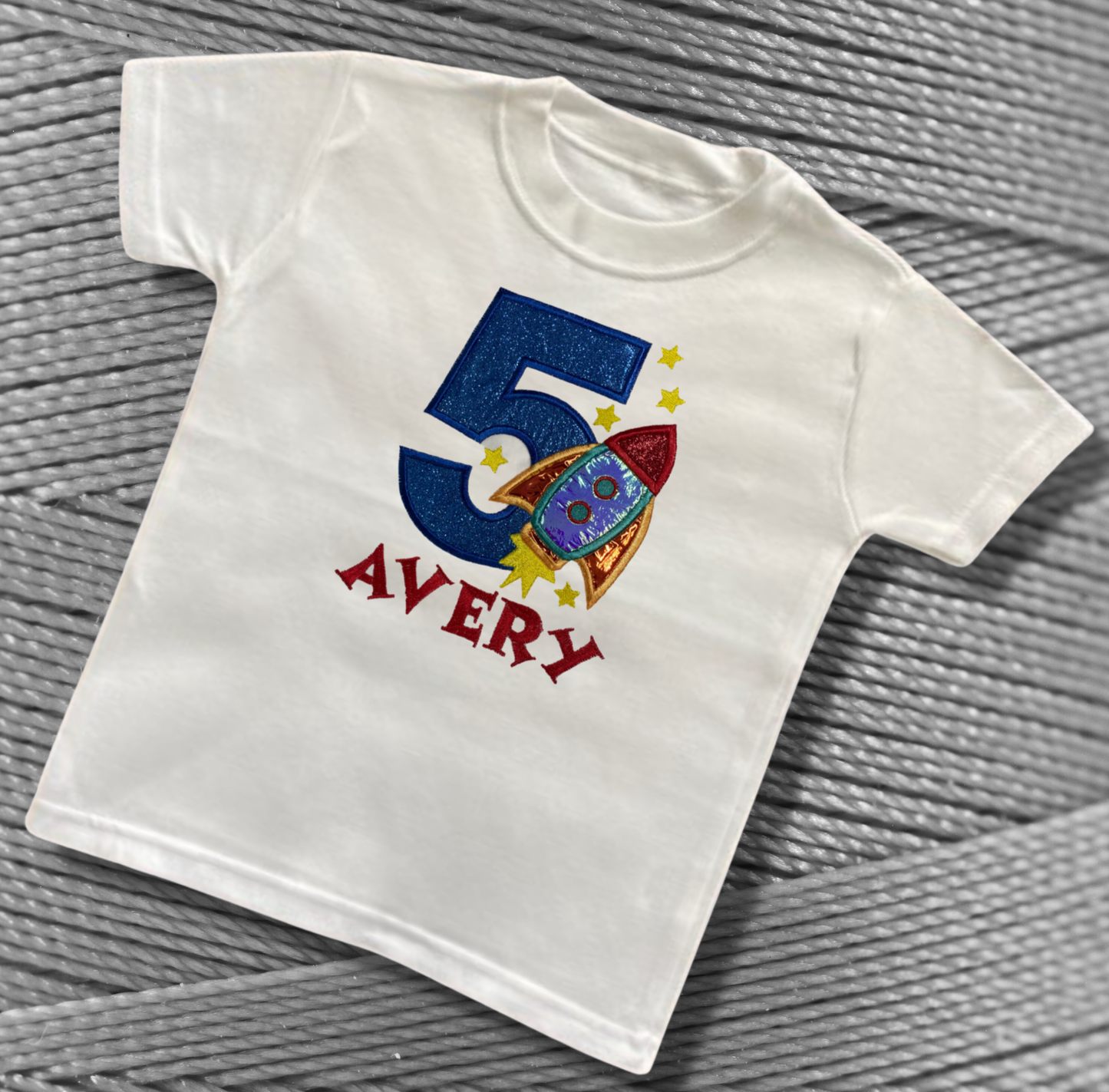 Childrens white soft cotton t-shirt. Embroidered applique on the front with the birthday age, rocket design and the childs name.