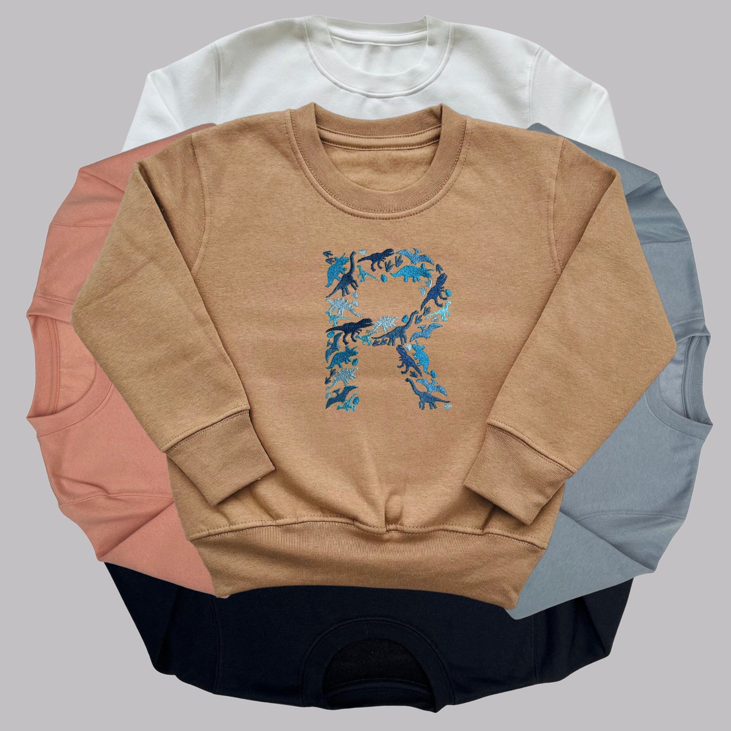 Personalised Embroidered Childrens Dinosaur Top. Dinosaurs in Beautiful Shades of Blue Make Up the Letter. A Perfect Gift for Dinosaur Fans.
