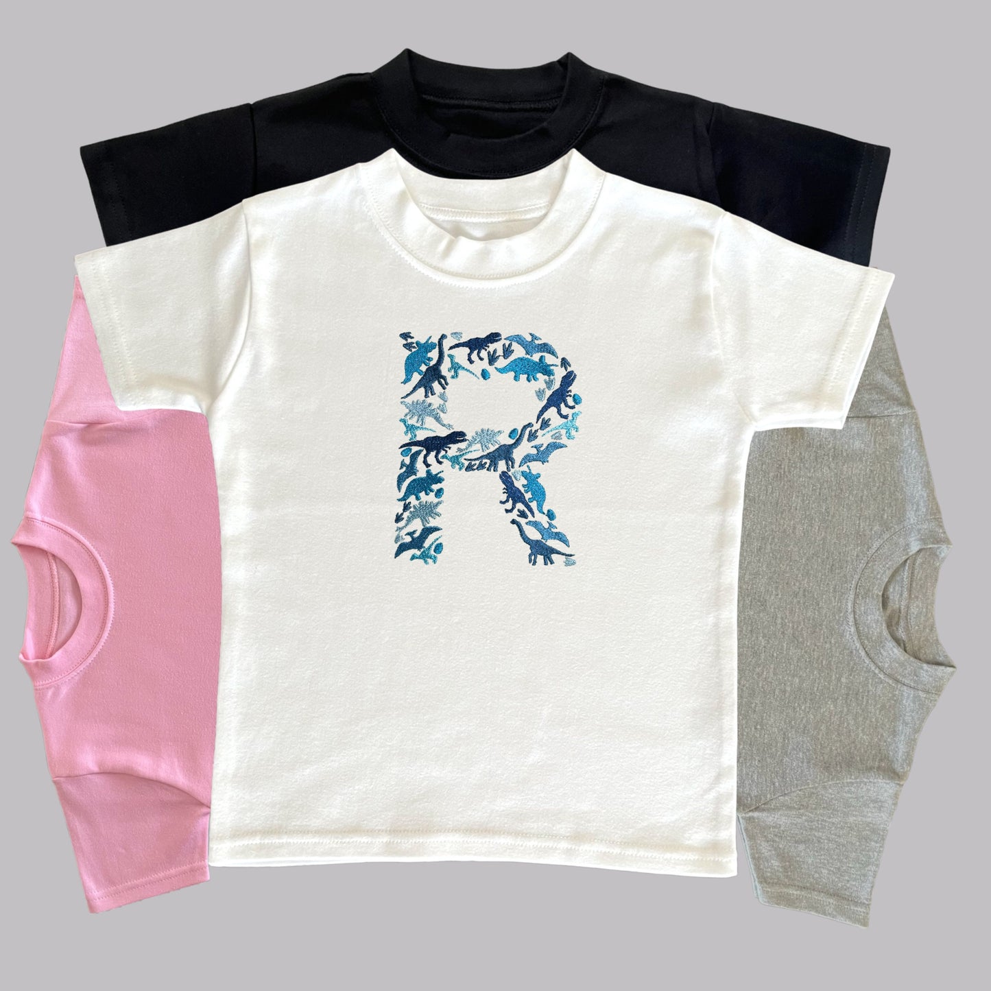 Personalised Embroidered Childrens Dinosaur Top. Dinosaurs in Beautiful Shades of Blue Make Up the Letter. A Perfect Gift for Dinosaur Fans.