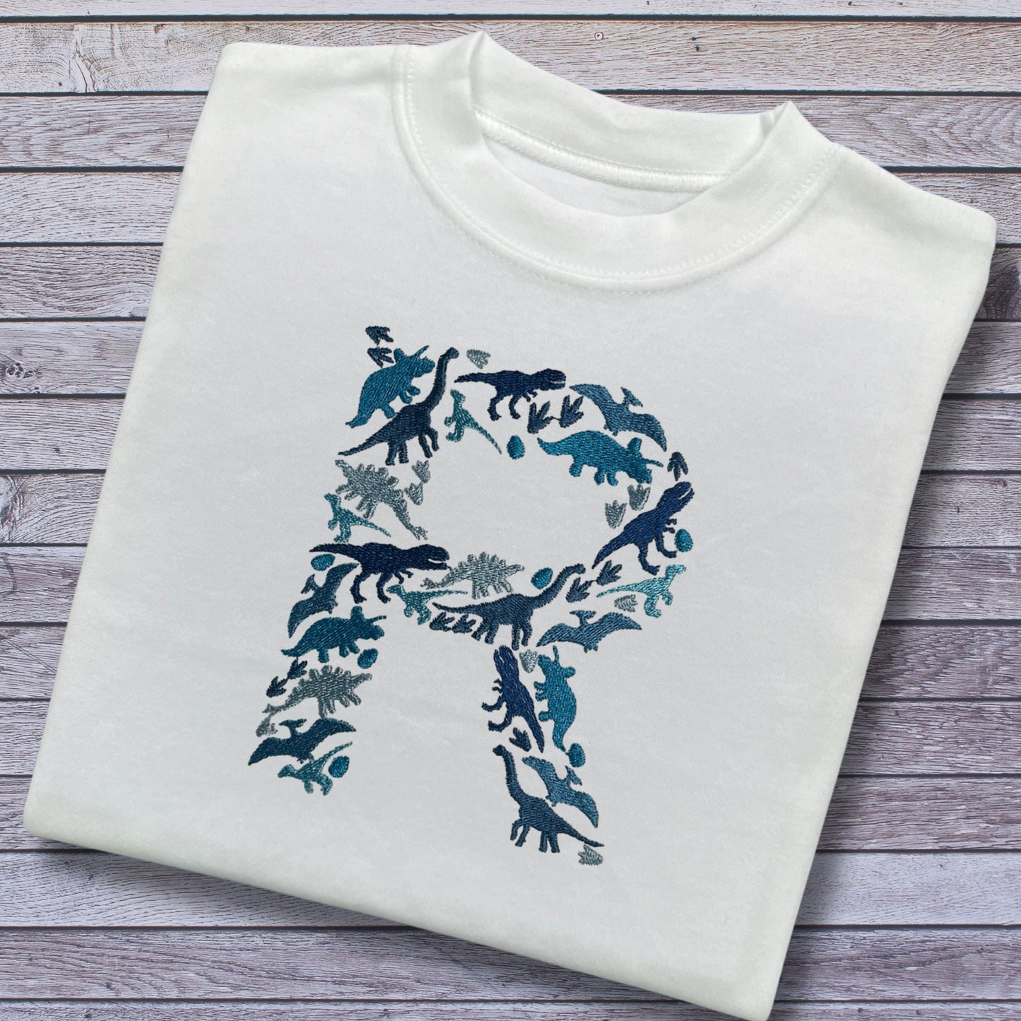 Personalised Embroidered Childrens Dinosaur Top. Dinosaurs in Beautiful Shades of Blue Make Up the Letter. A Perfect Gift for Dinosaur Fans.
