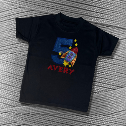 Childrens black soft cotton t-shirt. Embroidered applique on the front with the birthday age, rocket design and the childs name.