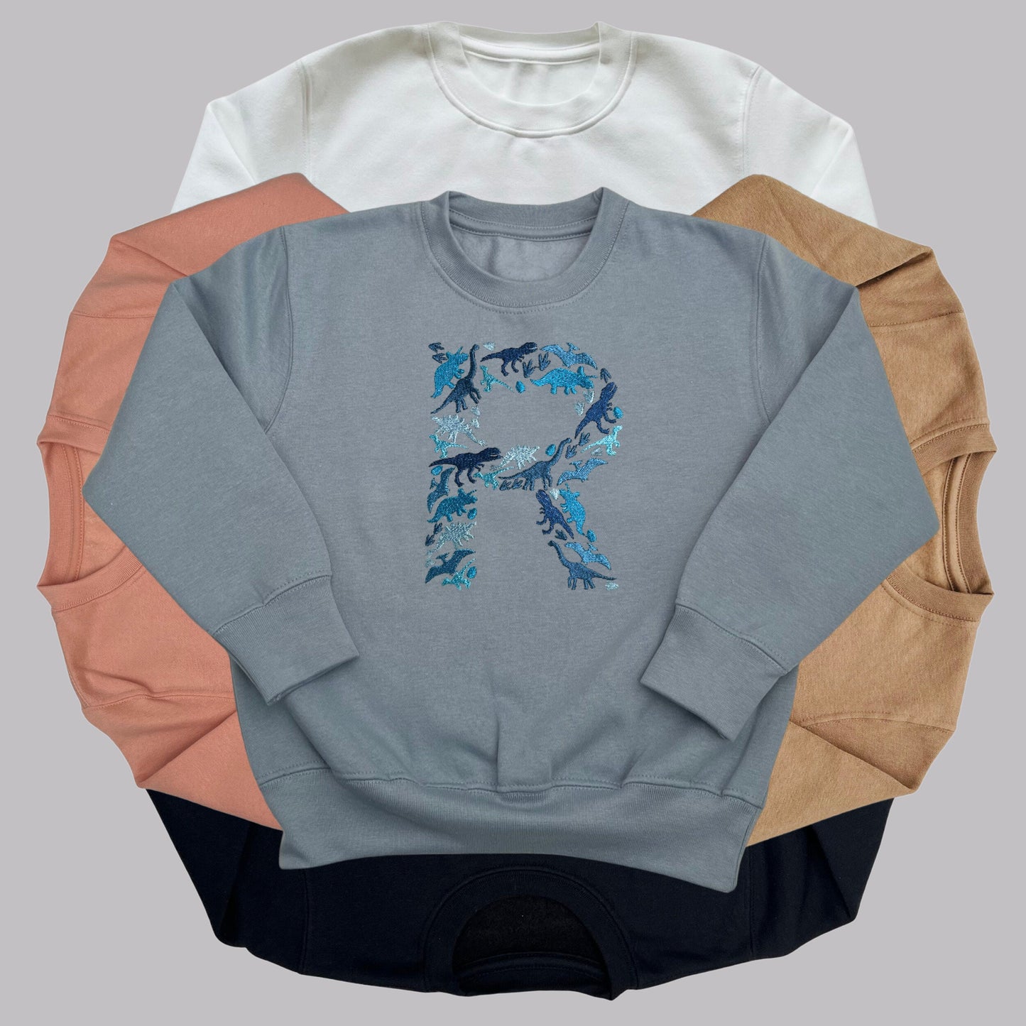 Personalised Embroidered Childrens Dinosaur Top. Dinosaurs in Beautiful Shades of Blue Make Up the Letter. A Perfect Gift for Dinosaur Fans.
