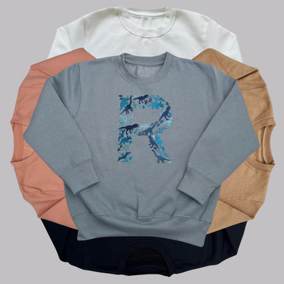 Personalised Embroidered Childrens Dinosaur Top. Dinosaurs in Beautiful Shades of Blue Make Up the Letter. A Perfect Gift for Dinosaur Fans.