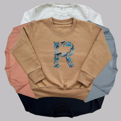 Personalised Embroidered Childrens Dinosaur Top. Dinosaurs in Beautiful Shades of Blue Make Up the Letter. A Perfect Gift for Dinosaur Fans.