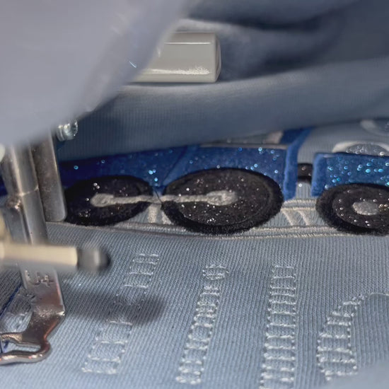 Embroidery machine stitching out the blue train design on a light blue sweatshirt