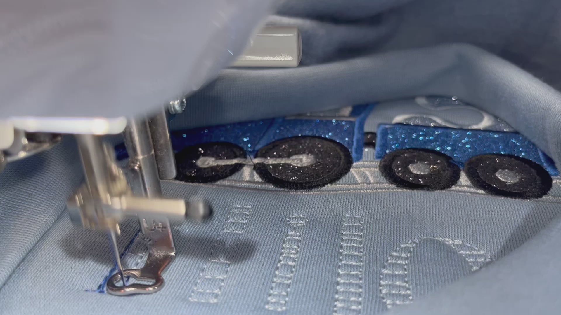 Embroidery machine stitching out the blue train design on a light blue sweatshirt